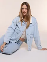 Campera de denim blanco de corte holgado con hombros caídos, cuello con solapa en contraste de color celeste, cierre frontal con botones metálicos y bolsillos delanteros con solapa.