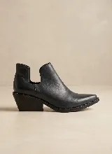 Botín de cuero negro con diseño de corte lateral y punta fina. Presenta un taco cuadrado de 5 cm y detalles de tachas metálicas en el borde de la suela.