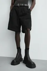 Bota tipo Chelsea de caña media, confeccionada en material sintético liso color negro. Presenta paneles elásticos laterales, tirador trasero y una suela robusta con plataforma track de gran volumen.