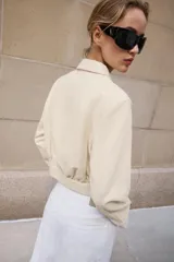 Camisa crop de manga larga con cuello solapa y cierre frontal de botones, confeccionada en tejido sintético con efecto piel color beige.