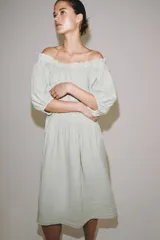 Vestido midi confeccionado en lino 100%, con escote recto elástico estilo hombros descubiertos, mangas abullonadas y detalle de pliegues en la cintura. Cuenta con bolsillos laterales ocultos y bajo asimétrico.