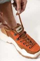 Zapatillas urbanas color óxido, con cordones marrones, suela gruesa blanca y detalles en cuero texturizado.