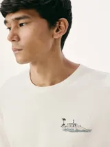 Camiseta blanca de algodón con cuello redondo y mangas cortas. Estampa rectangular con borde negro que contiene la frase "NATURAL ATMOSPHERE" en letras mayúsculas y una imagen de montañas y mar.