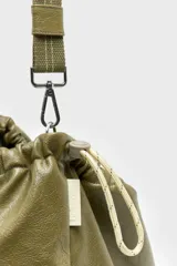 Bolso tipo hobo confeccionado en cuero vacuno color verde militar, con diseño fruncido en la parte superior y cierre con cordón ajustable. Cuenta con una correa larga regulable y desmontable sujeta por mosquetones metálicos.