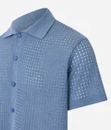 Camisa celeste de punto calado con cuello inglés, manga corta y abotonadura frontal.