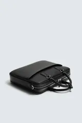 Maletín negro con textura grabada, diseño estructurado y asas de mano. Cuenta con cierre principal de cremallera, bolsillo frontal plano y bolsillo interior para dispositivos electrónicos de hasta 13 pulgadas. Incluye asa de hombro ajustable y extraíble.