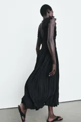 Vestido midi negro de escote pico y manga sisa, con detalles de bordados combinados a tono. Presenta un tejido plisado con efecto arrugado y cierre en la espalda con lazada y cremallera oculta.