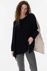 Poncho de tejido de punto con diseño oversize y tajos laterales. Presenta un frente en color negro y una espalda en color crudo, con cuello redondo y mangas largas.