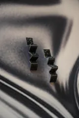 Par de aros colgantes con forma geométrica irregular, recubiertos de strass negros sobre base plateada.