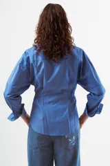 Camisa azul de algodón con finas rayas blancas verticales, cuello mao, manga larga y detalle de pinzas y botones en la zona de la cintura. Posee dos bolsillos de parche con tapa en el pecho.