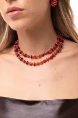 Collar doble de estilo artesanal, compuesto por cuentas de nácar teñidas en color rojo y discos de piedra hematite en tonos dorado y plateado. Incluye cadena de acero quirúrgico para ajuste de largo.