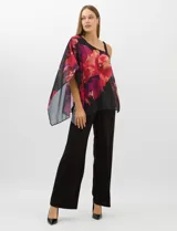 Enterito de seda fría con pantalón corte palazzo de pierna ancha. Presenta un diseño de un hombro descubierto con tirante fino y una sobrecapa asimétrica de gasa estampada con motivos florales en tonos rojos y fucsia sobre fondo negro que cae desde el hombro derecho.