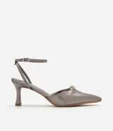 Zapato de tacón color gris con punta fina, tira fina con hebilla en el tobillo y detalle de nudo con strass.