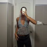 Top halter gris claro, ajustado al cuerpo, con escote pronunciado en V y cubierto de lentejuelas plateadas. El tejido es semitransparente.