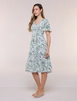Vestido midi de rayón con estampado de hojas en tonos verde oscuro y blanco. Cuenta con escote en V, pechera fruncida con punto smock, mangas cortas con detalles de pompones en los bordes y lazo ajustable en la cintura.