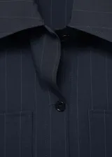 Camisa de corte recto con diseño de raya diplomática, cuello camisero, cierre frontal de botones y dos bolsillos de parche delanteros. Presenta mangas largas con puños rectos.