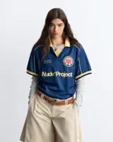 Remera de fútbol estilo vintage de la marca Nude Project, en color azul marino con cuello polo y detalles en amarillo. Presenta inscripciones y un escudo bordado en el pecho.