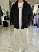 Campera puffer impermeable color beige con capucha desmontable con cordones negros, cierre frontal con cremallera y solapa con botones a presión.