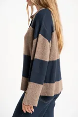 Sweater de tejido de punto color blanco roto o crema, con textura jaspeada. Presenta cuello polo y un escote con tres botones nacarados. El calce es holgado (oversize) y tiene mangas largas.