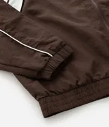 Campera deportiva de poliamida color marrón con detalles en blanco en los hombros y mangas. Presenta cierre frontal completo, cuello alto y puños elásticos.