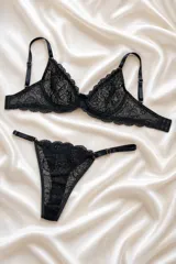 Conjunto de lencería negro de encaje floral, compuesto por un corpiño con aros y tirantes regulables, y una tanga regulable con laterales finos.