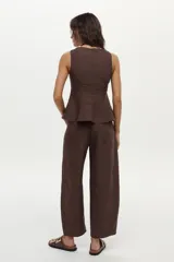 Top de lino color beige con cuello bote y diseño con peplum, sin mangas y con cierre invisible en la espalda.