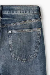 Jeans de cinco bolsillos en denim de algodón rígido, color azul medio con efecto desgastado y lavado. Modelo de cintura clásica con cierre de botón y corte relajado de cadera a bajo con pierna recta más amplia.