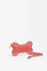 Monedero pequeño con forma de hueso, color rosado, con cierre de cremallera dorado y correa corta. Presenta el logo "BIMBA" estampado en el frente.