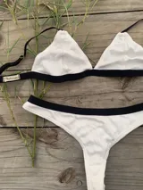 Conjunto de bikini bicolor blanco con detalles en negro, compuesto por un top triangular con tirantes regulables y una bombacha de tiro medio.