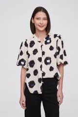 Blusa de manga corta con estampado de manchas negras y azules sobre fondo crema, cuello mao y cierre frontal con botones.