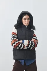 Chaleco puffer negro con diseño acolchado, capucha desmontable y cierre frontal. Cuenta con cordones ajustables en la cintura y bolsillos laterales.