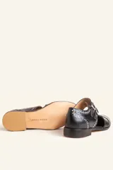 Zapato tipo oxford abierto en los laterales, confeccionado en cuero vacuno negro. Presenta doble tira con hebillas metálicas en el empeine y detalle de tachas plateadas en el contorno del talón y la puntera.
