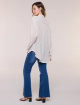 Camisa Magaschoni de silueta holgada y tejido texturizado color blanco, con cuello camisero, cierre frontal de botones, mangas largas con presilla para arremangar y diseño asimétrico con espalda más larga.