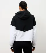 Campera rompeviento deportiva con diseño bicolor en negro y blanco. Presenta capucha con cordón ajustable, cierre frontal y puños elásticos.