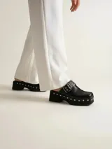 Zueco de cuero encerado color negro, con diseño de punta cuadrada, detalle de tachas metálicas en el lateral y hebilla ajustable en la capellada. Cuenta con suela de goma.