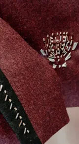 Chaqueta corta verde oscuro de paño, con cuello mao, hombros fruncidos con mangas abullonadas y cierre frontal de botones dorados. Presenta detalles de bordados dorados en el frente y puños con tajo.