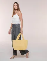 Cartera tipo shopper color amarillo de textura soft y flexible, con doble asa superior fija y compartimento principal amplio con botón metálico.