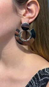 Caravanas de diseño geométrico en color plateado, compuestas por un círculo superior pequeño y una pieza inferior en forma de semicírculo que rodea un aro central.