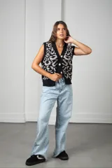 Chaleco de punto con diseño animal print en tonos gris y negro, con cuello en V y borde frontal en color rojo vibrante. Presenta cierre frontal con botones grandes y corte holgado.