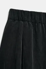 Pantalón fluido de tiro medio color verde militar, con cintura elástica en la parte trasera, pinzas en el delantero y bolsillos laterales ocultos en la costura. Presenta un diseño de pernera ancha y corte tobillero, con cierre frontal de cremallera y botón.