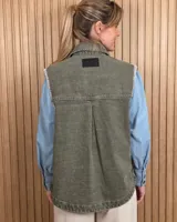 Chaleco de denim color marrón, confeccionado en 100% algodón, con bolsillos frontales amplios, cierre de botones y costuras decorativas bordadas en blanco en los bordes y los bolsillos.