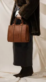 Cartera estructurada de tamaño mediano, confeccionada en símil cuero color negro. Presenta doble asa de mano, correa larga ajustable y desmontable, y un bolsillo trasero con cierre. El compartimento principal cuenta con cierre, división interna y bolsillos organizadores.
