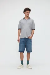 Remera polo de manga corta gris claro, con cuello y puños en gris oscuro, media cartera de botones, tajos laterales y bordado sutil de la marca en el pecho.