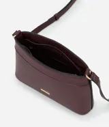 Cartera bandolera pequeña de formato rectangular, confeccionada en poliuretano con acabado liso. Presenta una correa larga ajustable, cierre superior con cremallera y un pequeño aplique metálico dorado con el logo de la marca en el frente.