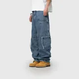 Pantalón de jean estilo cargo con corte ultra baggy y diseño de paneles. Presenta bolsillos laterales tipo cargo con bordes deshilachados y costuras reforzadas. Confeccionado en denim de algodón con textura rústica.