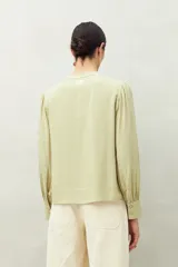 Camisa celeste de manga larga con cuello redondo y escote en V. Presenta detalles de pasamanería en el frente y las mangas, y botones forrados al tono. De corte fluido.