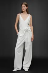 Pantalón blanco de tiro alto con trabillas, bolsillos laterales y falsos bolsillos de vivo en la espalda. Incluye cinturón lazada en el mismo tejido.