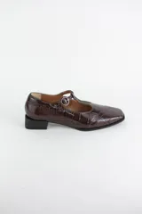 Zapatos estilo Mary Jane de cuero con acabado acharolado y textura efecto croco en color marrón oscuro. Presentan punta cuadrada, cierre con tira en el empeine y taco cuadrado bajo.