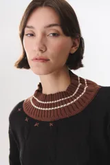 Buzo de tejido de punto con diseño de trenzas, color crema con detalles en marrón en cuello, puños y ruedo. Presenta líneas finas en contraste y pequeñas costuras decorativas en forma de cruz.
