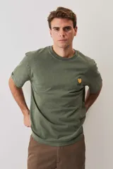 Remera de calce relajado y cuello redondo, color verde musgo con efecto lavado, y pequeño bordado de un morrón en el pecho.